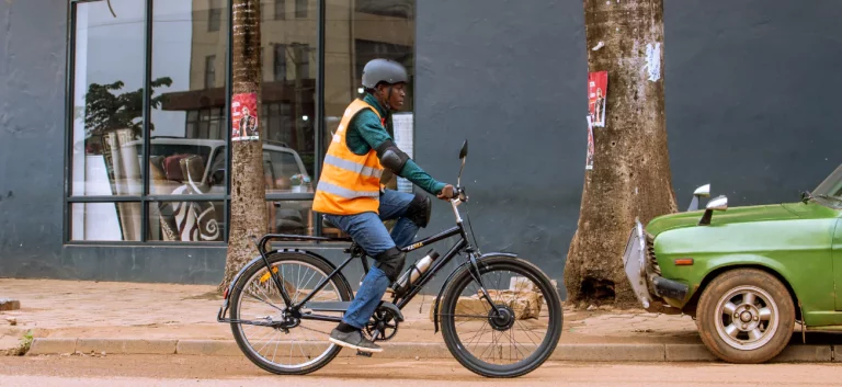A rider in a hi-vis vest on a Karaa e-bike outside a shop in Kampala
