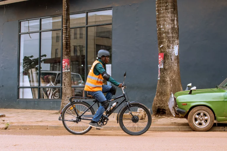 A rider in a hi-vis vest on a Karaa e-bike outside a shop in Kampala